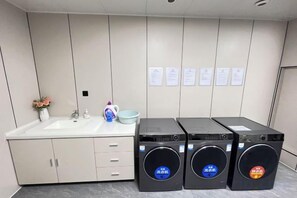 A hotel bathroom with a sink, mirror, and three black washing machines. - Fengleyuan Hotel (Zhengzhou)