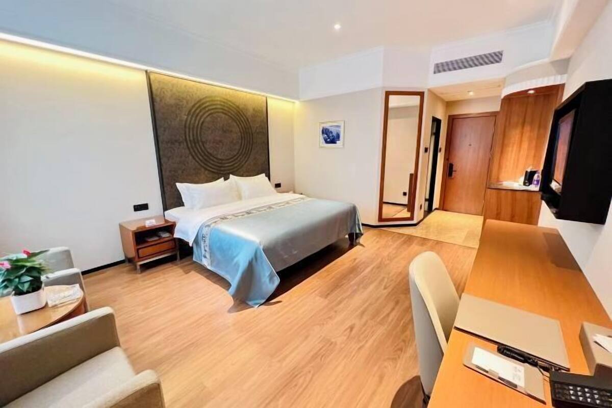 A modern hotel room with a neatly made bed, a wooden desk with a computer, a chair, and a TV.