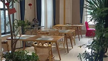 A dining area with wooden tables and chairs, a potted plant, and a red chair.