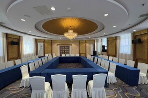 A conference room with a long table, white chairs, and a chandelier. - Fengleyuan Hotel (Zhengzhou)