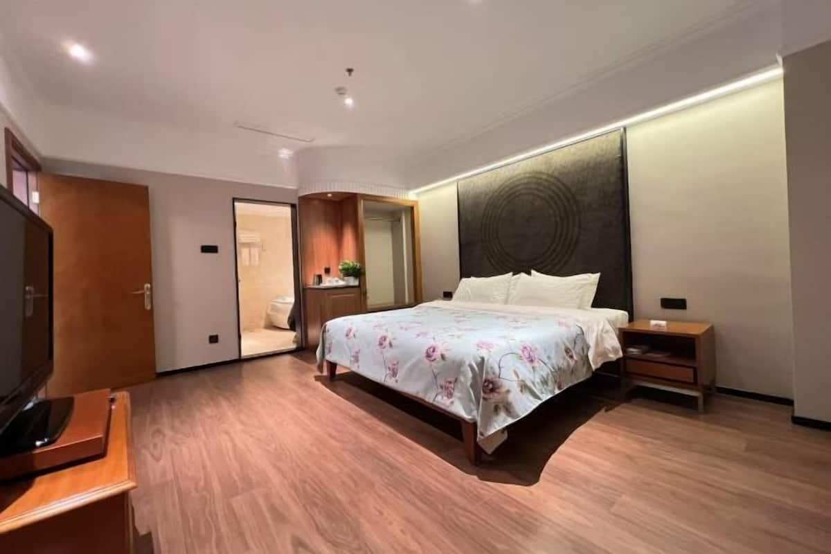 A modern bedroom with a wooden floor, a bed with floral bedding, a nightstand, a TV, and a mirror.