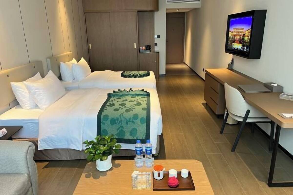 A hotel room with two beds, a desk, a TV, and a small seating area.