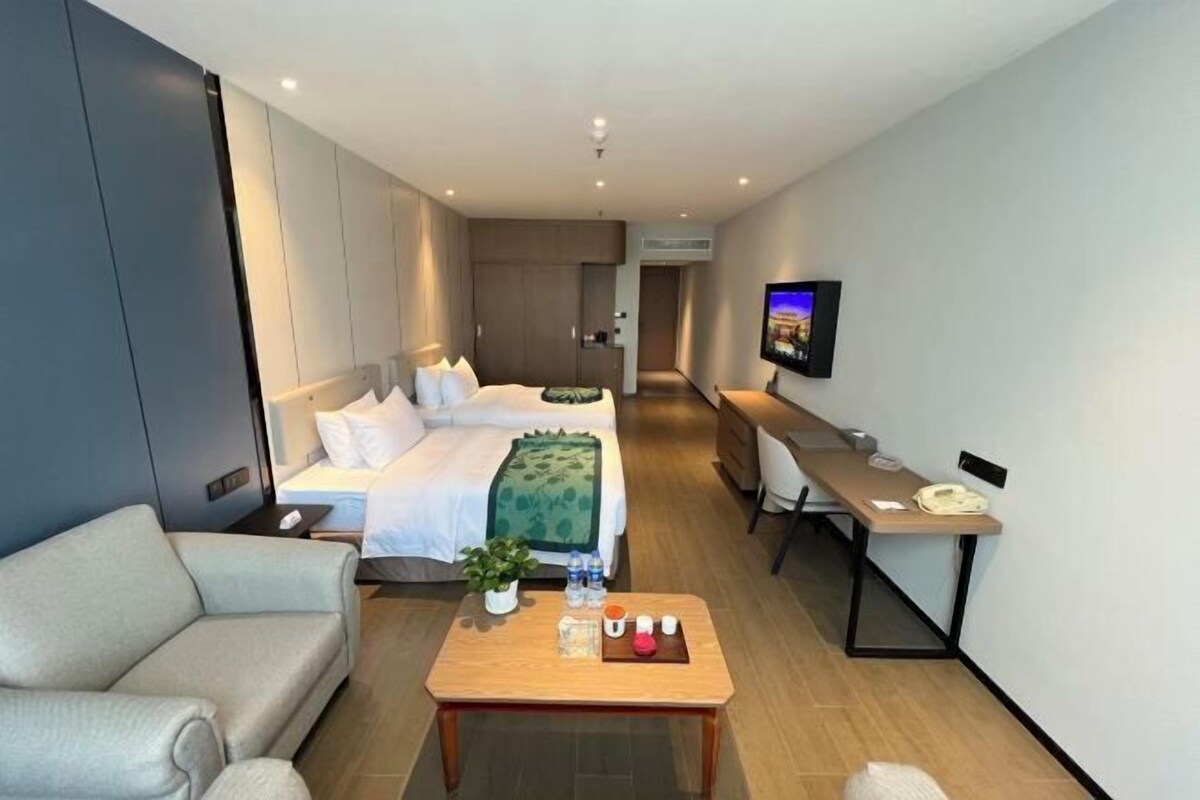 A modern hotel room with a bed, a sofa, a desk, a TV, and a coffee table.