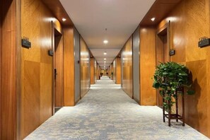 A hotel corridor with wooden paneling, a patterned carpet, and a potted plant. - Fengleyuan Hotel (Zhengzhou)