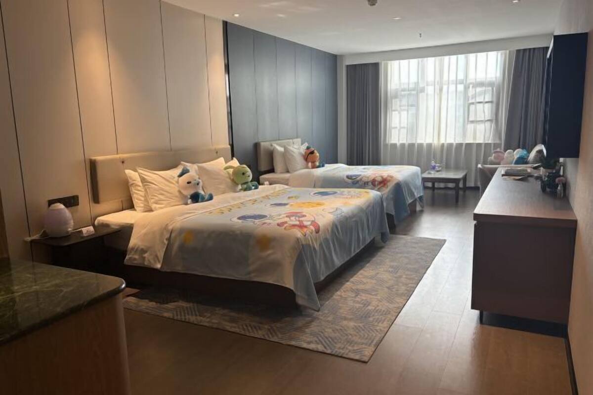 A hotel room with two beds, a desk, and a large window with curtains.
