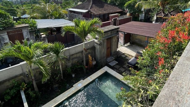 A pool surrounded by lush greenery and palm trees, with a view of distant mountains and a cloudy sky. - Blue Royal Amed (Karangasem)