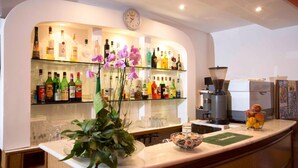 A bar area with shelves of liquor bottles, a clock, a coffee machine, and a plant with purple flowers. - Hotel veliero (Rimini)