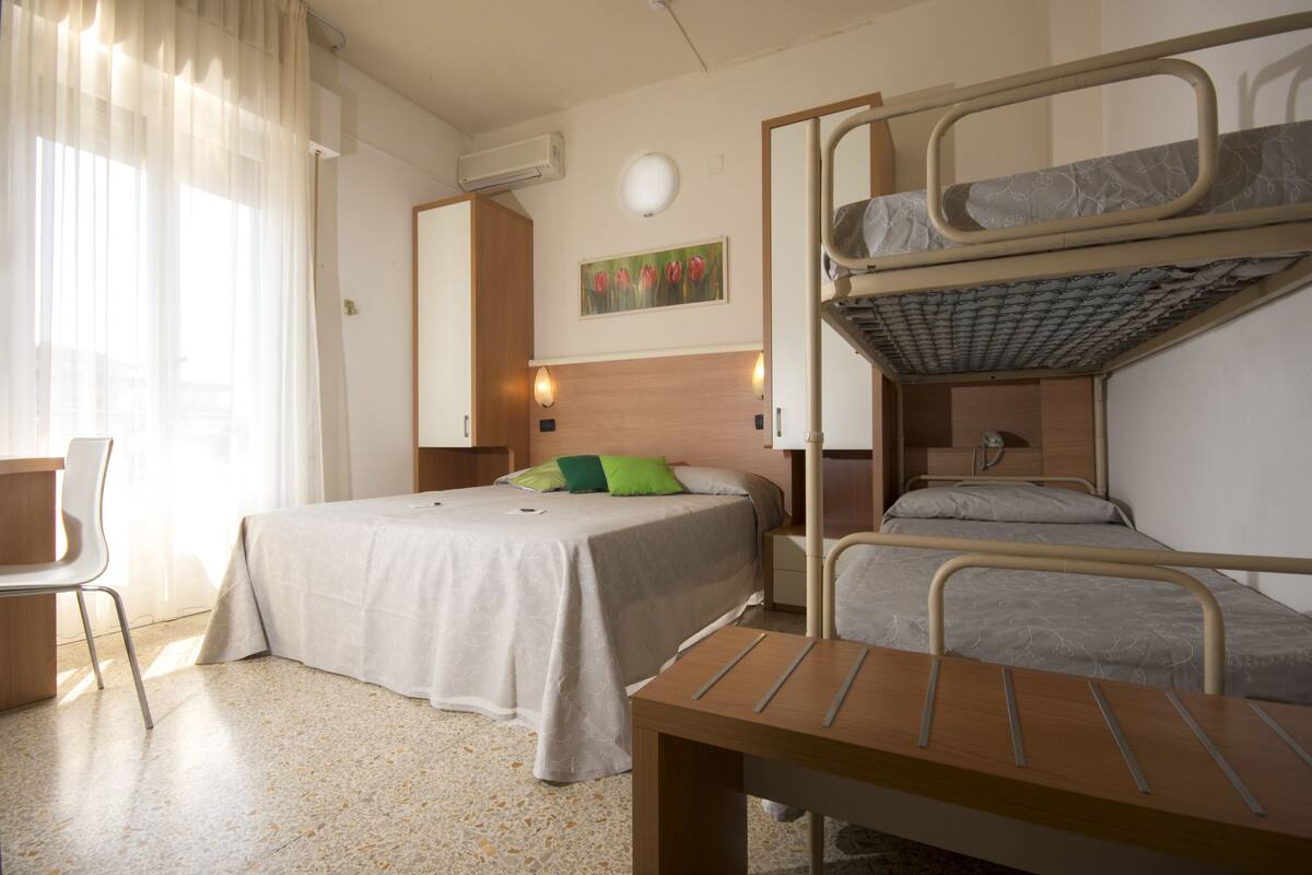 Une chambre d’hôtel avec des lits superposés, un bureau, une chaise et un lit avec un oreiller vert.