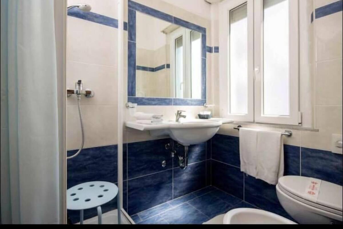 Une salle de bain équipée d’un lavabo, d’un miroir, de toilettes et d’un petit tabouret rond.
