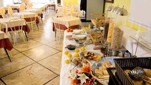 A buffet setup with various food items, including fruits, bread, and beverages, arranged on a table in a dining area with chairs and tables. - Hotel veliero (Rimini)