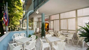 A spacious indoor patio with white plastic chairs and tables, large windows, and a view of the outside. - Hotel veliero (Rimini)