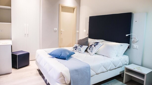 A modern bedroom with a bed, bedside tables, a wardrobe, and a mirror. - Hotel veliero (Rimini)
