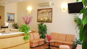 A hotel lobby with a reception desk, sofas, a coffee table, and wall-mounted TV. - Hotel veliero (Rimini)