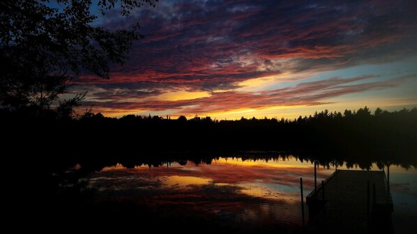 A sunset over a calm lake with a dock and trees silhouetted against the sky.
