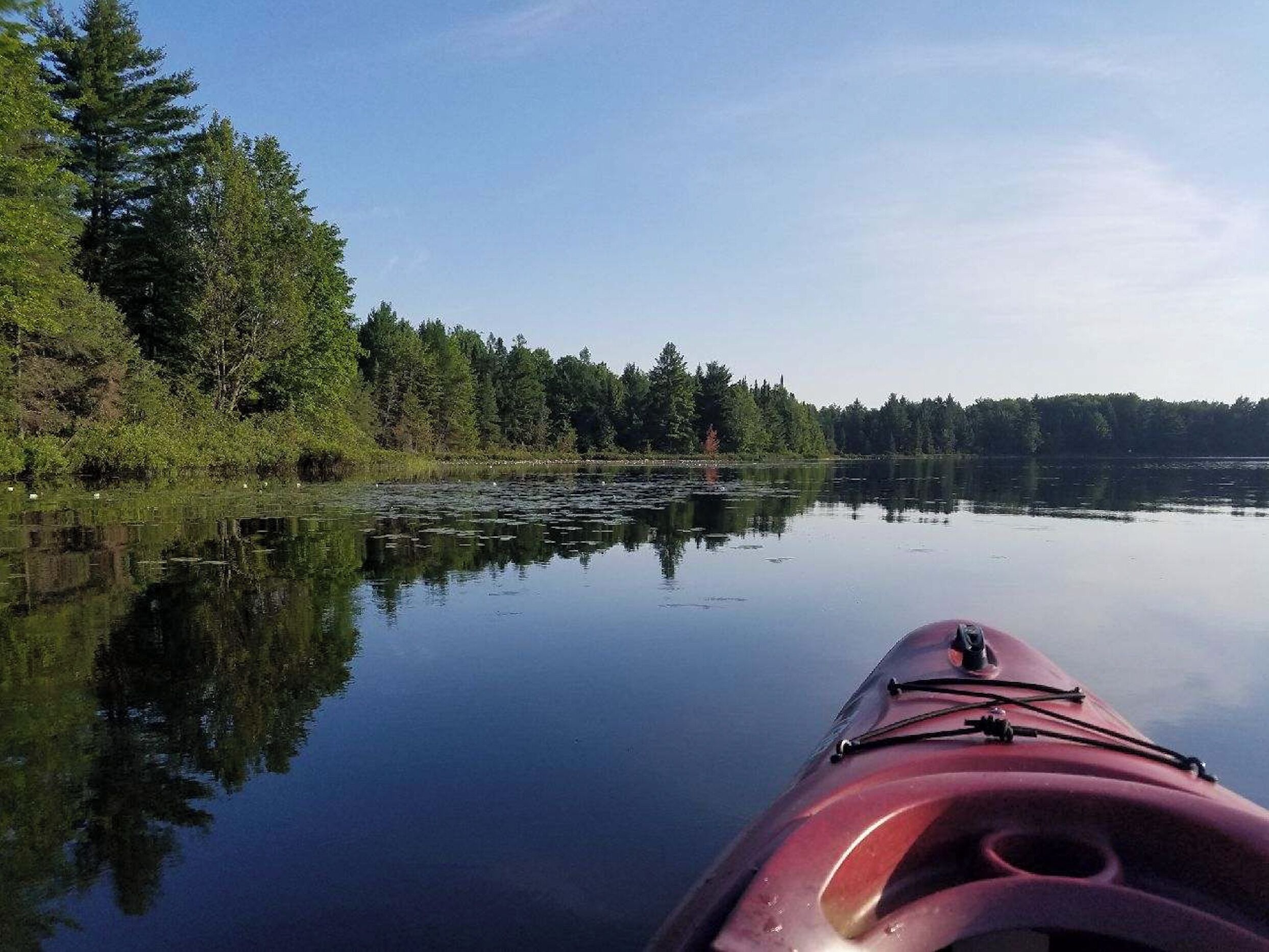 Un lago tranquilo con un kayak rojo en primer plano, rodeado de un bosque denso.