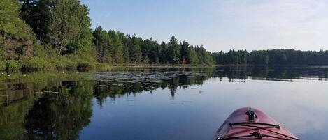 Un lago tranquilo con un kayak rojo en primer plano, rodeado de un bosque denso.