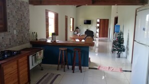 A kitchen with a bar area, wooden stools, a refrigerator, a TV mounted on the wall, and a Christmas tree. - Ximenes and Daubian House (Bonito)