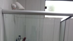 A small, tiled shower area with a glass door, a shelf with toiletries, and a blue decorative tile border. - Ximenes and Daubian House (Bonito)