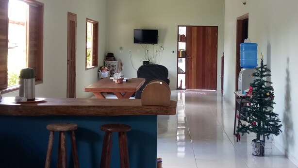A spacious living area with a high ceiling, a wooden ceiling structure, a kitchen area with a counter and stools, a television mounted on the wall, and a small Christmas tree. - Ximenes and Daubian House (Bonito)