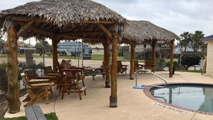 Un espace piscine doté de chaises longues en bois et de petits pavillons à toit de chaume.