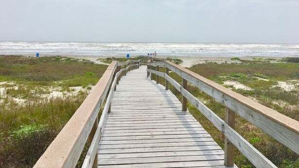 Une promenade en bois menant à une plage bordée de dunes, sous un ciel nuageux.