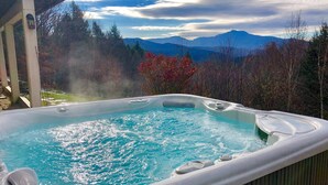 A hot tub with a mountain view, surrounded by trees and a wooden deck.