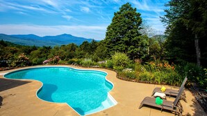 A swimming pool with a curved edge, surrounded by lush greenery and a view of mountains.