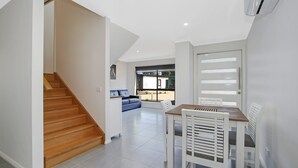 A modern interior with a wooden staircase, a dining area with a table and chairs, and a blue sofa in the background. - BrightAway - Located in Bright, Victoria (BRIGHT)