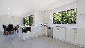 A modern kitchen with white cabinets, a dishwasher, a microwave, and a large window offering a view of trees. - BrightAway - Located in Bright, Victoria (BRIGHT)