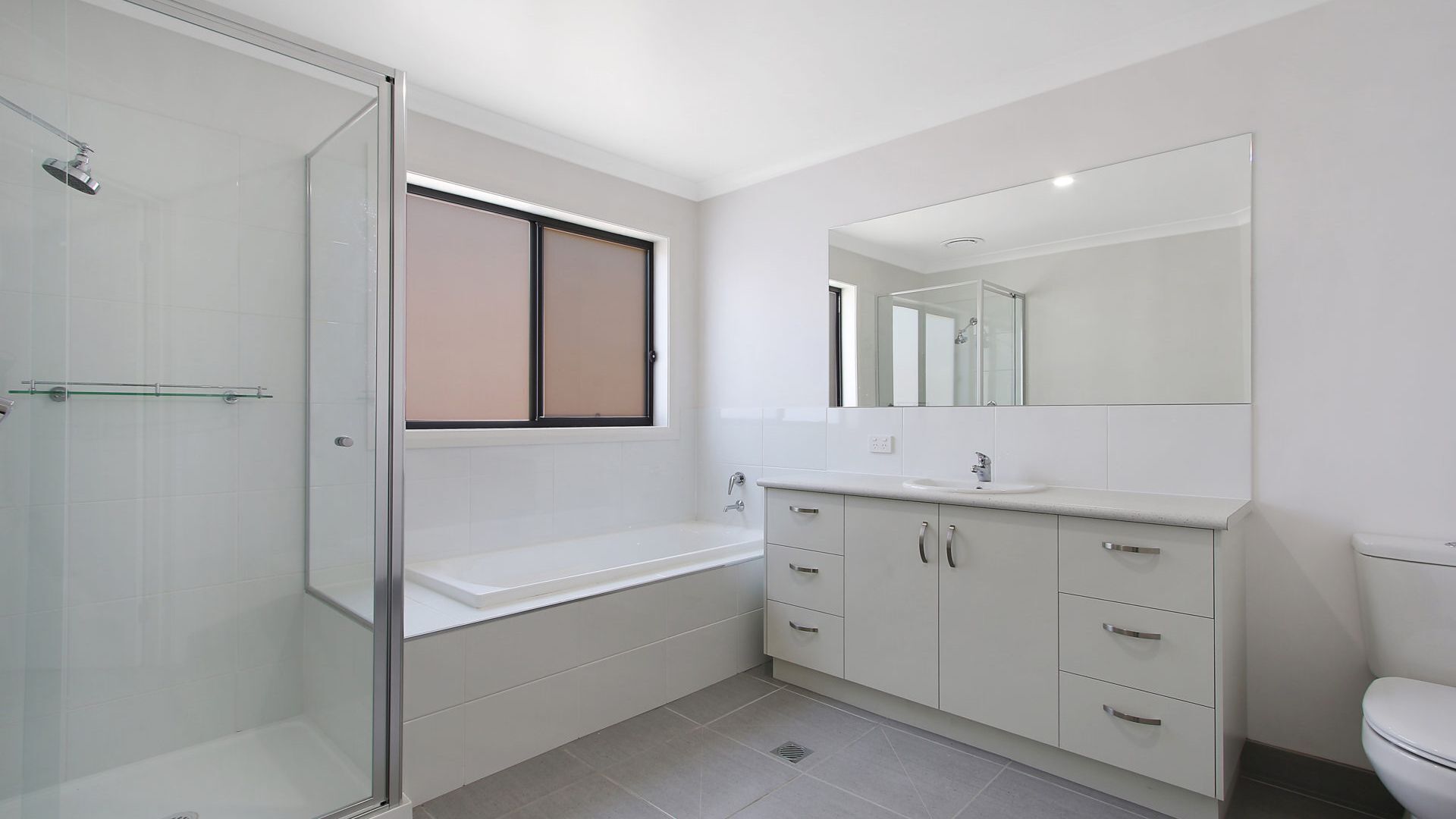Une salle de bain moderne avec une douche à parois de verre, un grand miroir et un meuble-lavabo blanc doté de tiroirs.