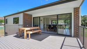 A modern house with a wooden deck, a dining area with a table and chairs, and a glass door leading to a balcony. - BrightAway - Located in Bright, Victoria (BRIGHT)