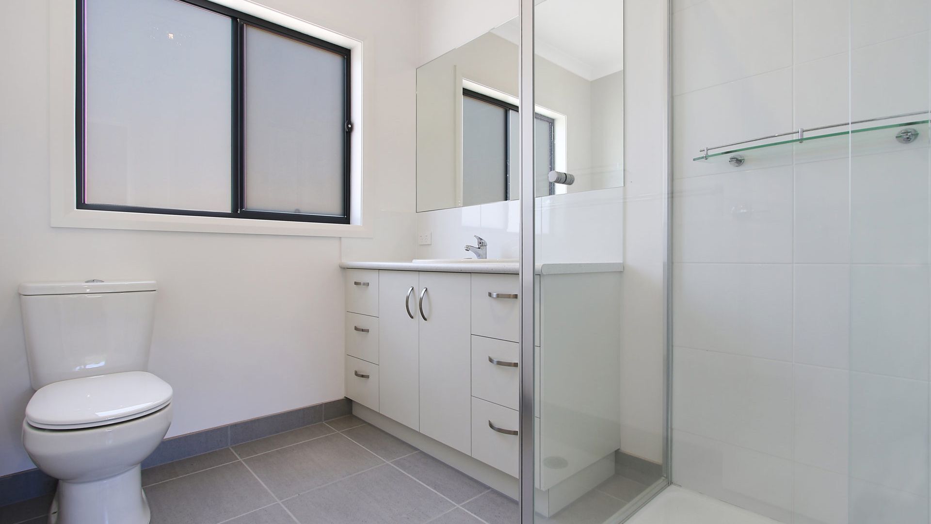 A bathroom with a toilet, a sink with a mirror, and a shower area.