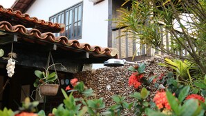 A garden with a variety of plants and flowers, a hanging plant, and a decorative wall made of shells. - BOAT HOUSE - Charm and Comfort on Geribá Beach (Búzios)