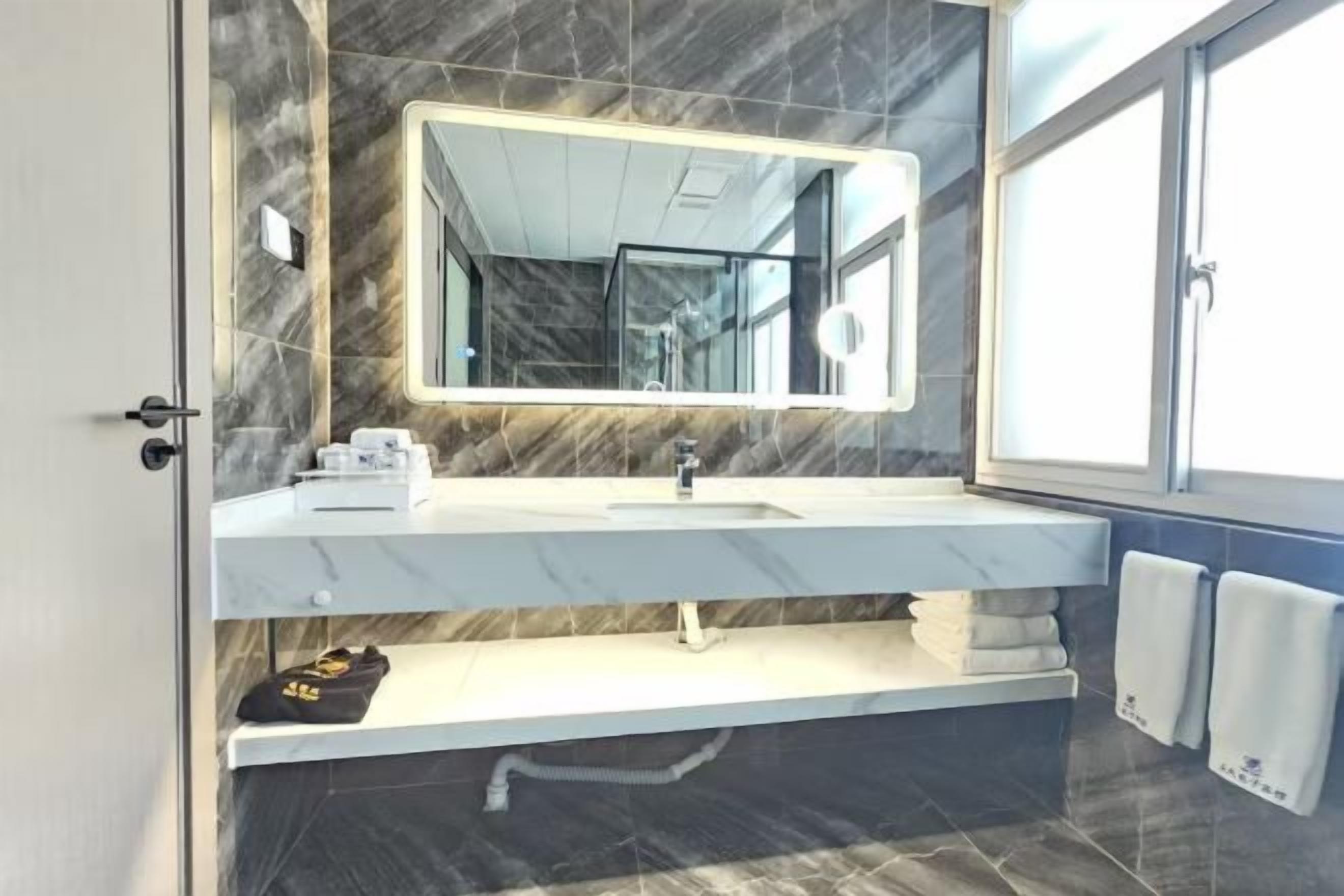 A modern bathroom with a marble vanity, a large mirror, and a window providing natural light.