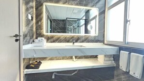 A modern bathroom with a marble vanity, a large mirror, and a window providing natural light.