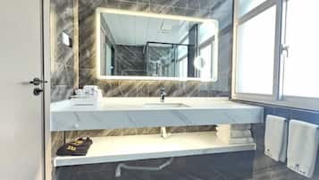 A modern bathroom with a marble vanity, a large mirror, and a window providing natural light.