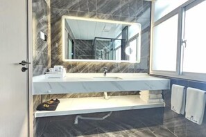 A modern bathroom with a marble vanity, a large mirror, and a window providing natural light.