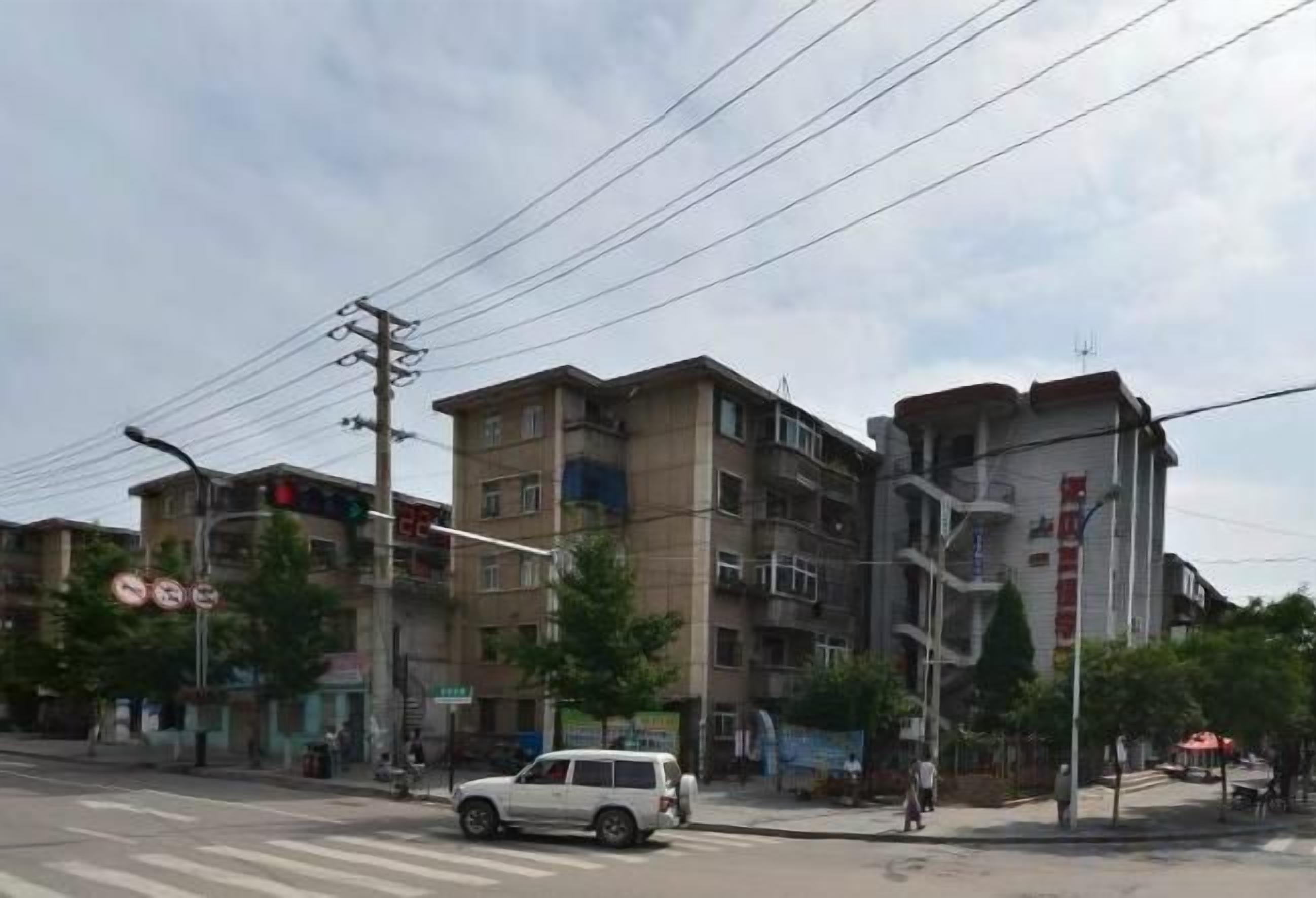Un edificio de varios pisos con una escalera, un paso de peatones y un vehículo blanco.