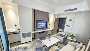 A modern hotel room with a flat-screen TV mounted on the wall, a small round table, a sofa, and a floral-patterned carpet. - Hua Tian Hotel (Tianshui)