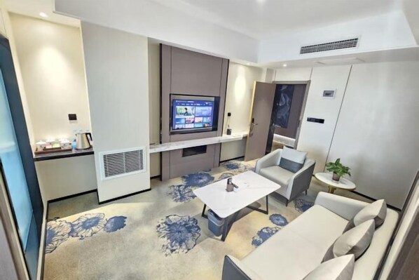 A modern hotel room with a flat-screen TV mounted on the wall, a small round table, a sofa, and a floral-patterned carpet. - Hua Tian Hotel (Tianshui)
