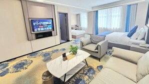 A modern hotel room with a flat-screen TV, a sofa, a bed, and a small table with a plant.