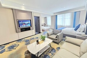 A modern hotel room with a flat-screen TV, a sofa, a bed, and a small table with a plant.