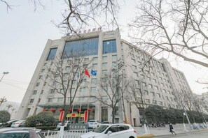 Un immeuble à étages doté d’une architecture moderne, avec une entrée imposante surmontée d’un mât portant un drapeau.