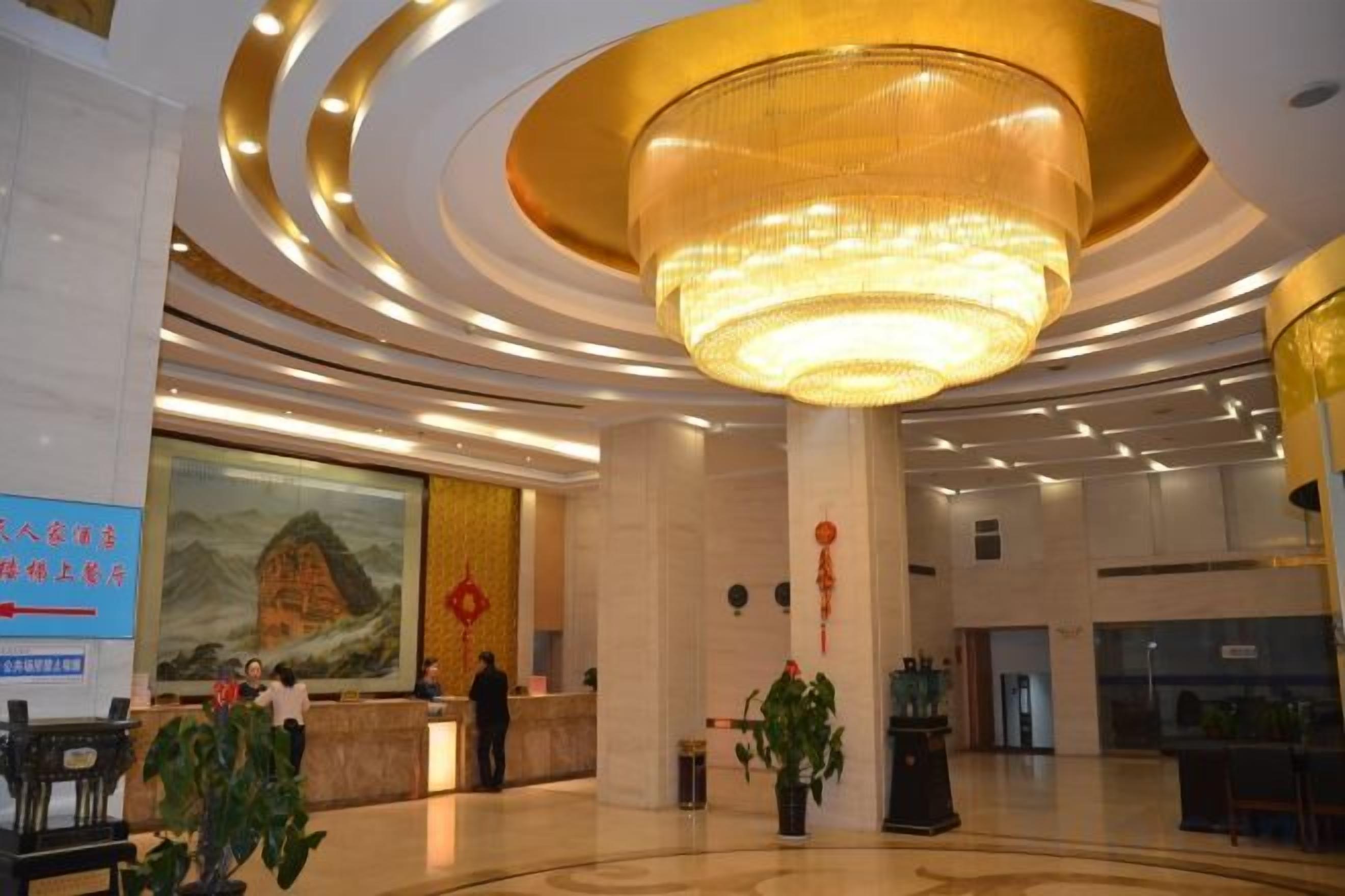 A hotel lobby with a large chandelier, reception desk, and a mural on the wall.