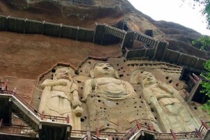 Grandes estatuas de Buda talladas en un risco, con una escalera que conduce hacia ellas.