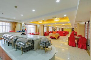 Un amplio comedor con mesas y sillas redondas, estaciones de buffet y una araña.