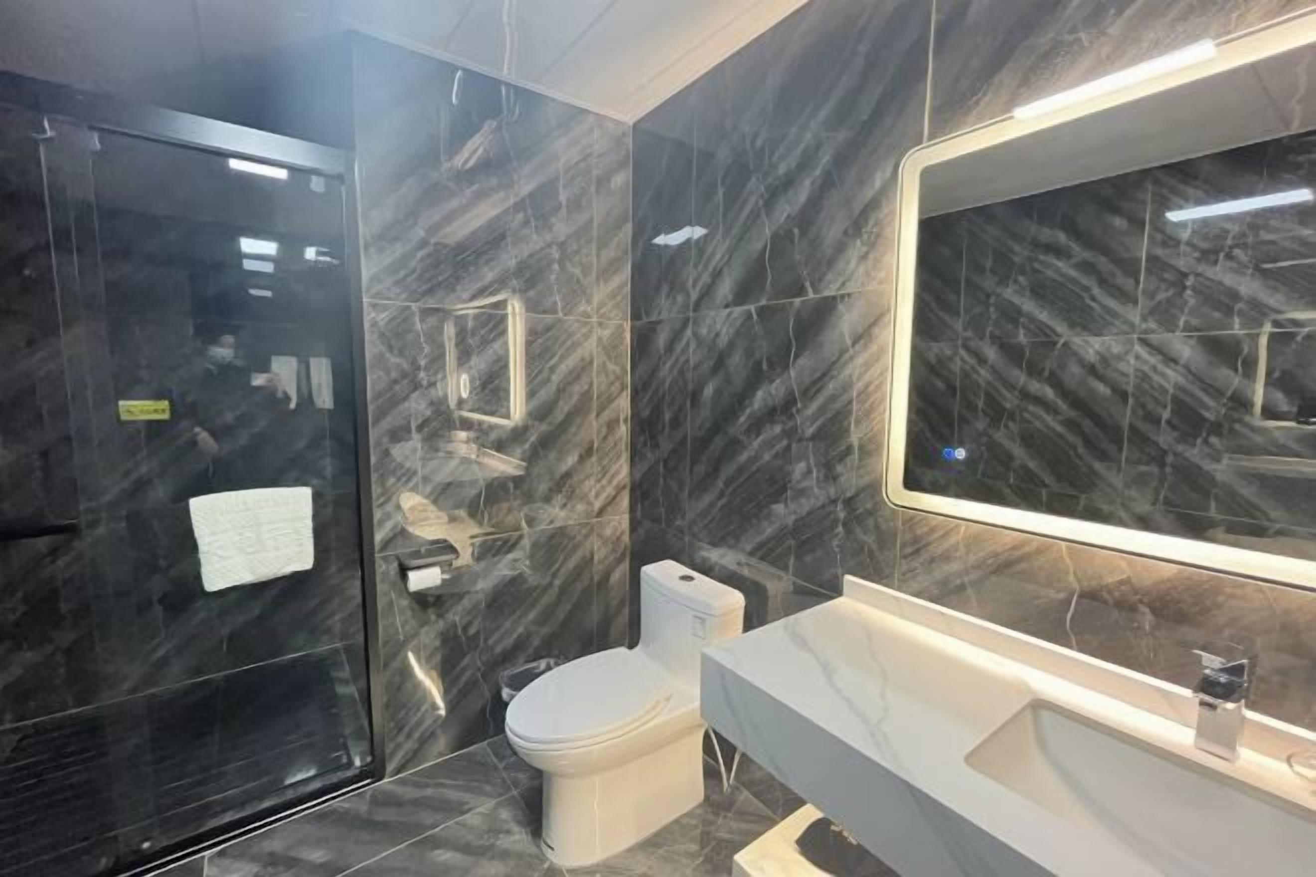 Ein modernes Badezimmer mit Marmorwand, Toilette in Weiß und einem großen Spiegel über dem Waschbecken.