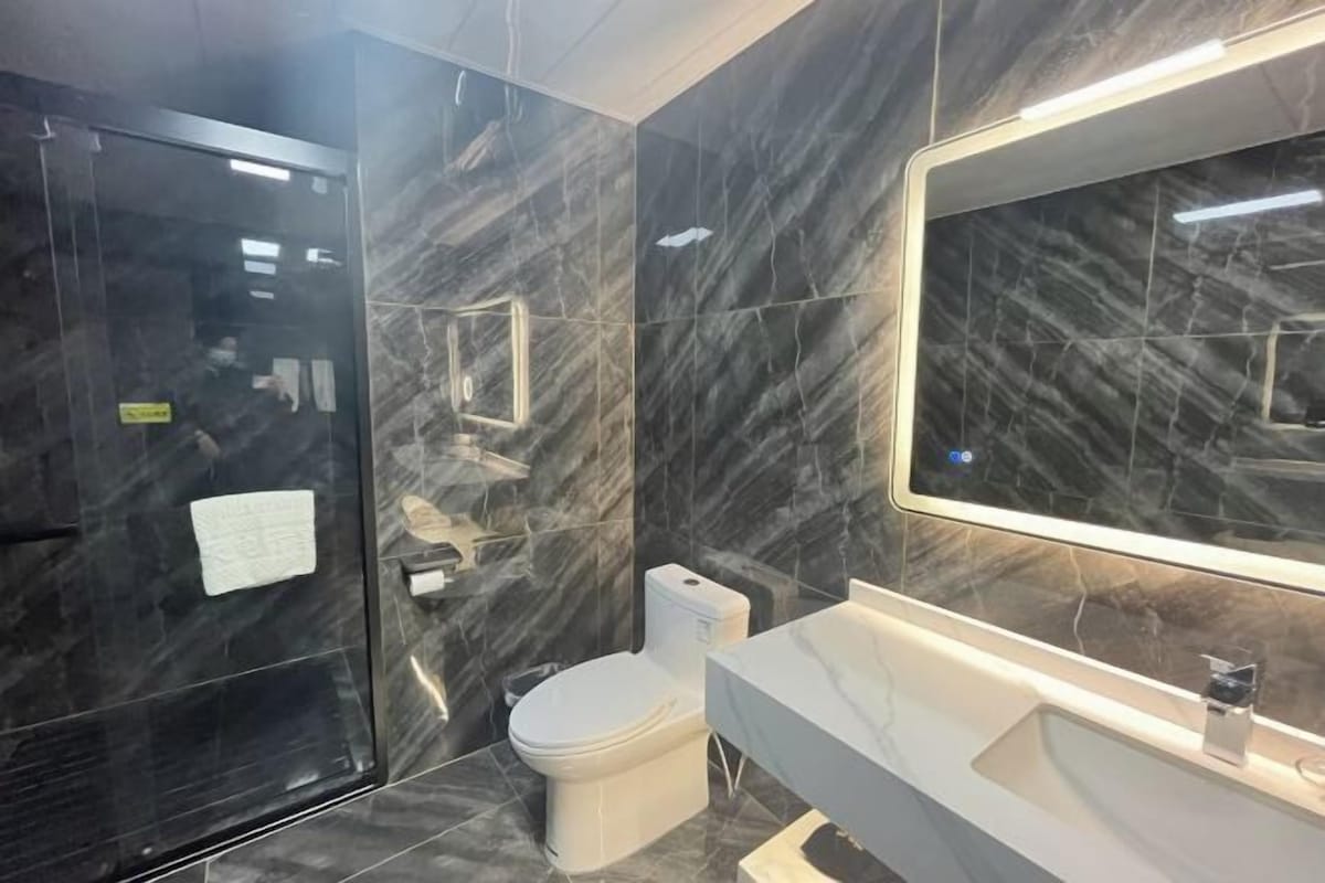 Un baño moderno con pared de mármol, inodoro blanco y un espejo grande sobre el lavamanos.