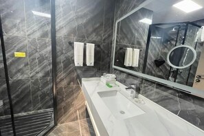 A modern bathroom with a white sink, a large mirror, and a shower area.