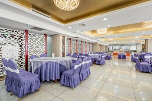 Un salón de banquetes con mesas redondas, sillas cubiertas de púrpura y paneles decorativos en la pared.